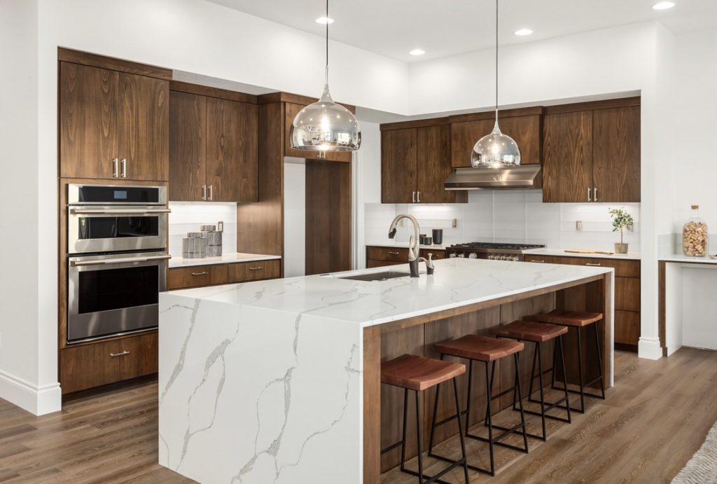 Kitchen in new luxury home with quartz waterfall island, hardwood floors, dark wood cabinets, and stainless steel appliances.