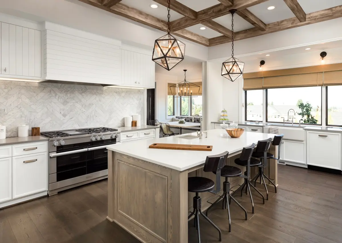 Kitchen Interior with Island, Sink, Cabinets, and Hardwood Floors in New Luxury Home. Features Elegant Pendant Light Fixtures, and Farmhouse Sink next to Window